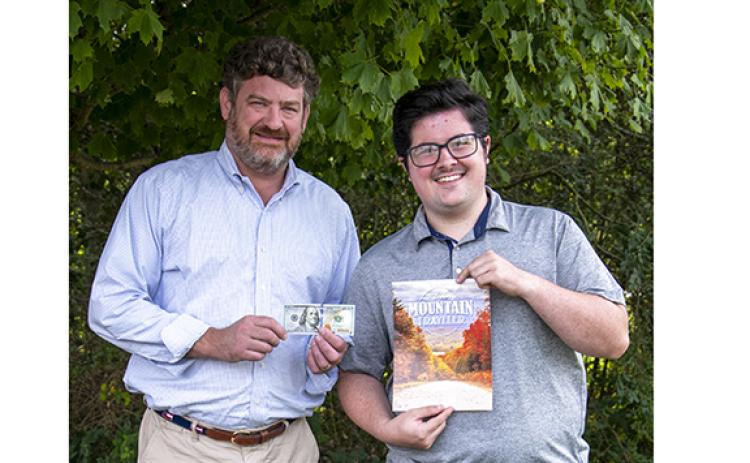 Clarkesville resident Carter Benton receives his $100 prize from Alan NeSmith, Community Newspapers Inc. chairman. Benton’s photo of a street in The Orchard subdivision ablaze with fall colors will grace the cover of the 2023 fall edition of The Mountain Traveler magazine. (Photo/Kimberly Brown)